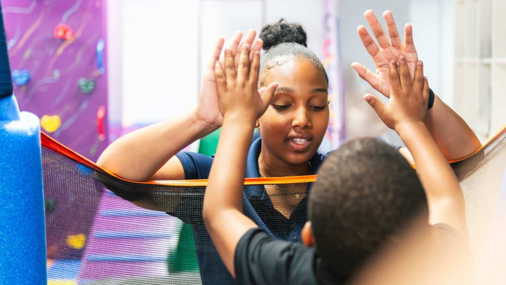 Iep For Autism: How Schools Create Individualized Support For Children With Autism Aba therapist raises her hands during an interactive activity with a young boy in a colorful sensory play area during an aba therapy session