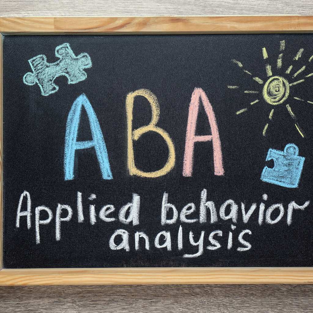 Blackboard with colorful chalk text reading 'aba applied behavior analysis' and puzzle piece drawings, representing aba therapy