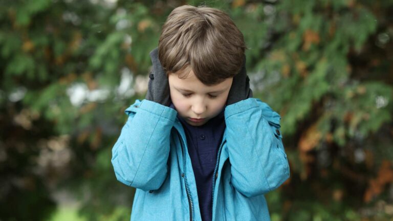 Child outdoors covering ears with hands, highlighting sensory sensitivity and the risks of untreated autism on daily comfort