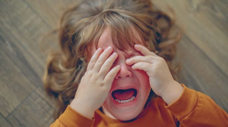 Child crying on the floor with hands over face, representing tantrums vs. meltdowns in kids with autism and the difference between a tantrum and a meltdown.