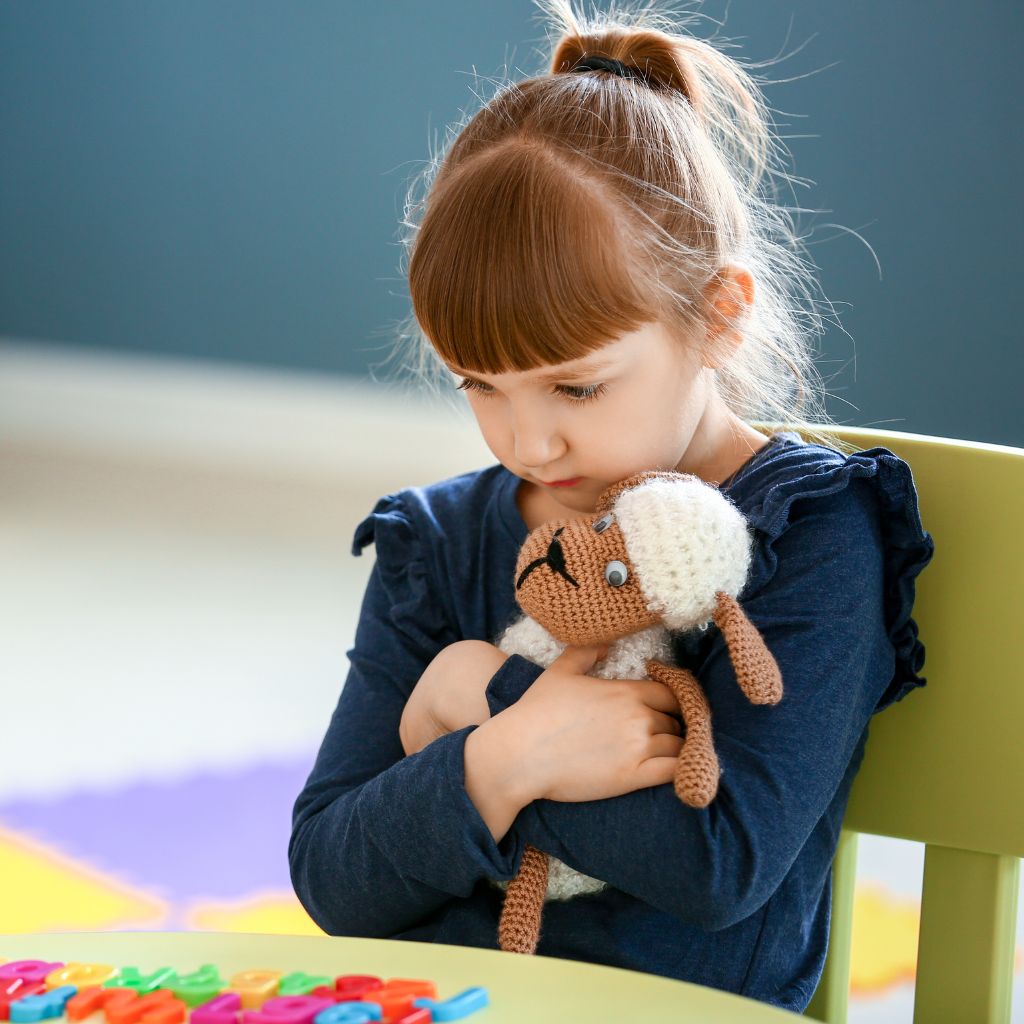 Young child hugging stuffed toy, looking pensive—illustrating early signs that may prompt an autism assessment.