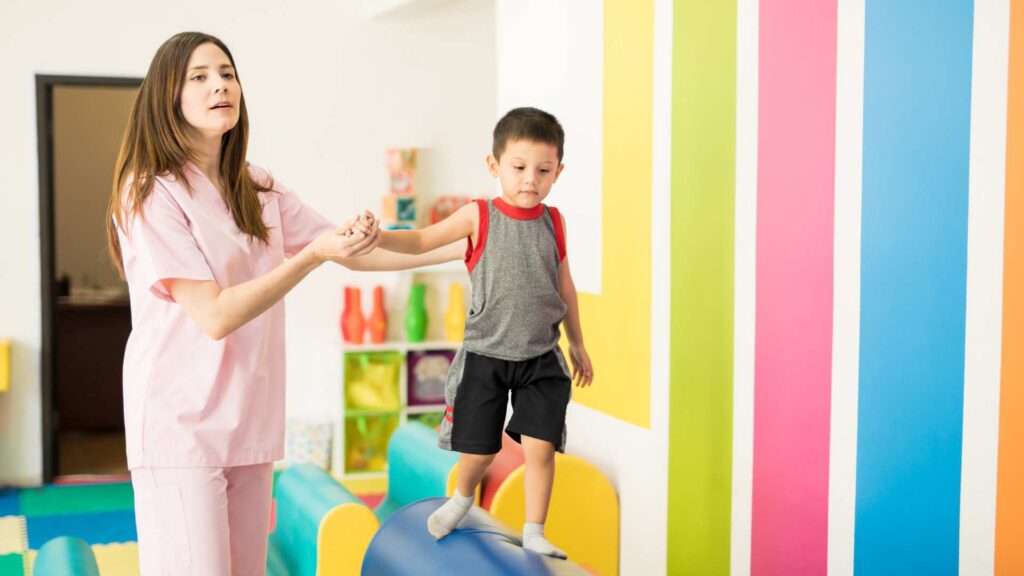 Aba Therapy Progress: What Does It Look Like And Why It'S Not Always Linear? Aba therapist supporting a child during a balance and motor skills activity meant to measure aba therapy progress